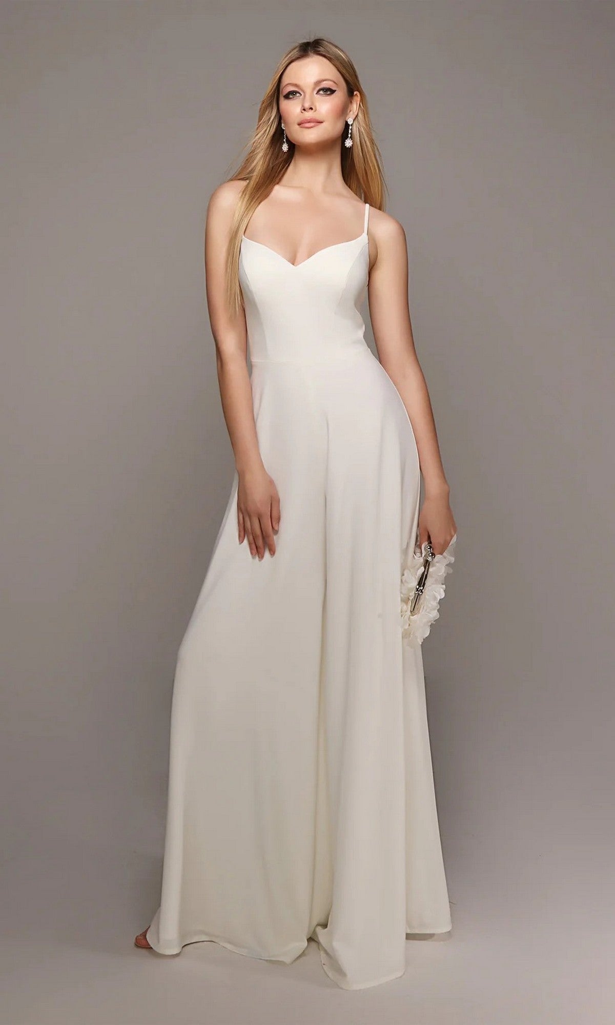 A woman models the Long White Jumpsuit: Alyce 70022, sleeveless and ivory, holding a clutch against a plain gray background.